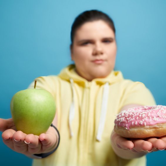 Close up of apple and donut keeping chunky brunnete girl