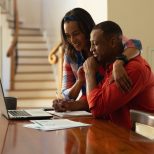 Smiling young african american couple planning home budget while sitting with laptop at table